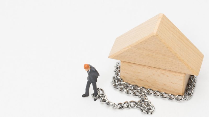 A visual representation of mortgage prisoners: a figure of a man chained to a toy house.