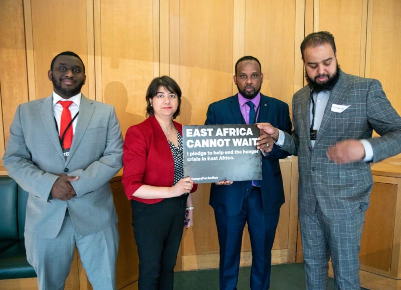 Seema, Mustafa and Daud hold a sign reading "East Africa cannot wait"