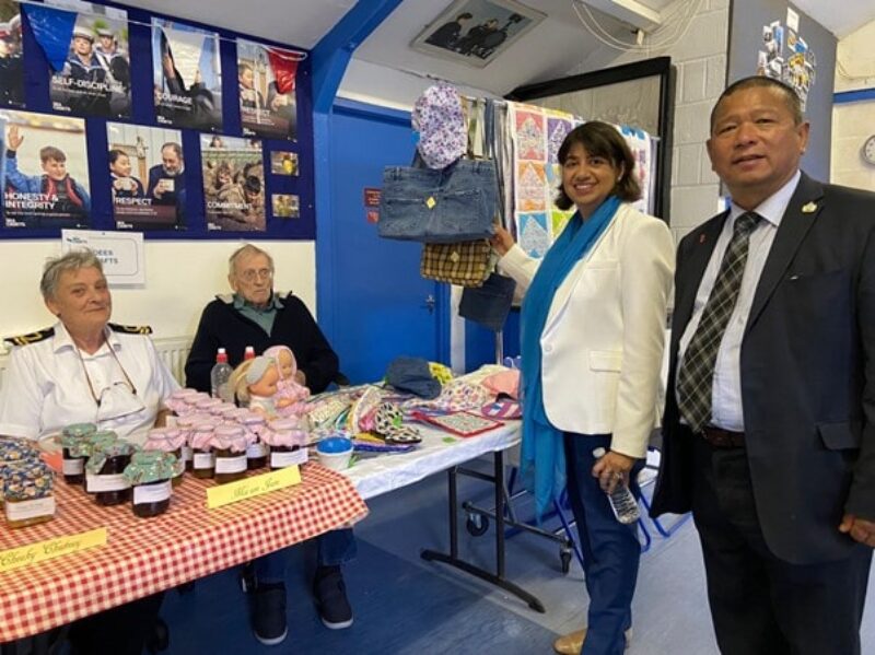 Seema Malhotra MP and Cllr Bahadur Gurung stand in front of stalls at the Hounslow and Feltham Sea Cadets Summer Extravaganza, where they are selling clothes along with jars of jam and chutney