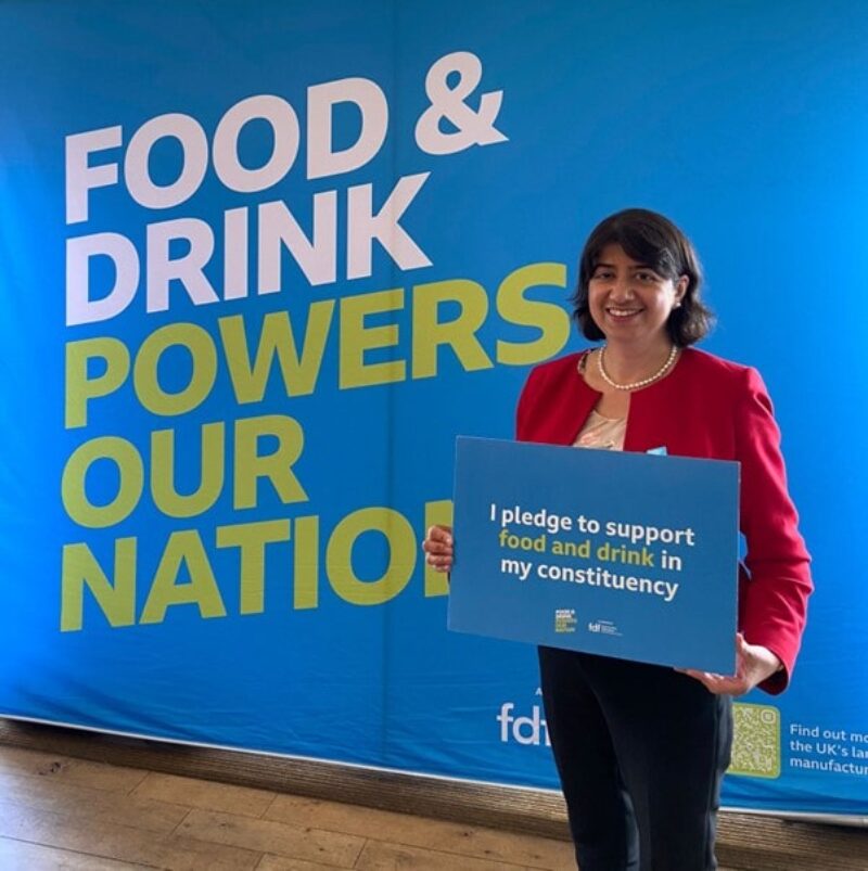 Seema Malhotra MP standing in front of a wall saying "Food & drink powers our nation". She holds a sign saying "
